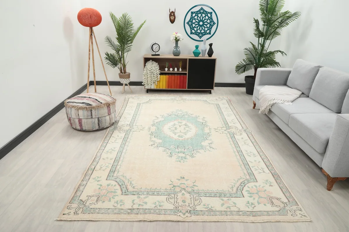 Large cream and green vintage rug in a living room setting with a sofa and plants