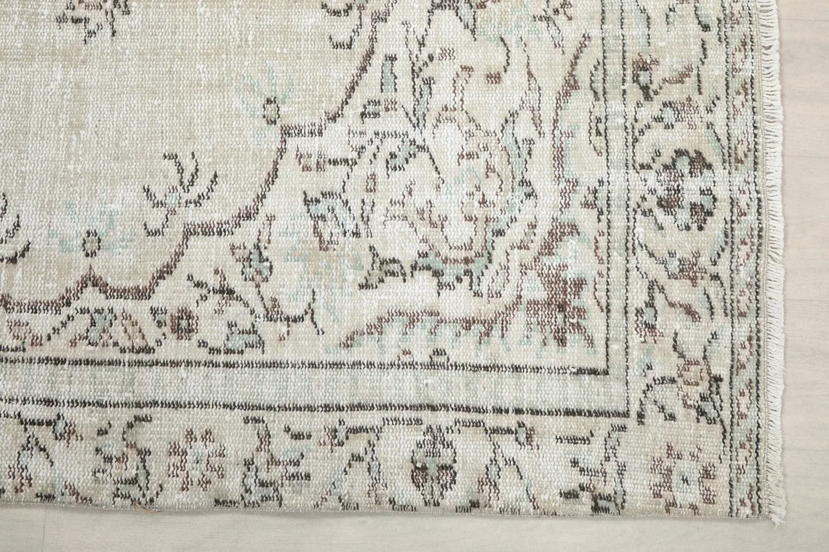 Detail view of the corner and border design of the ivory rug, showing charcoal and green tones
