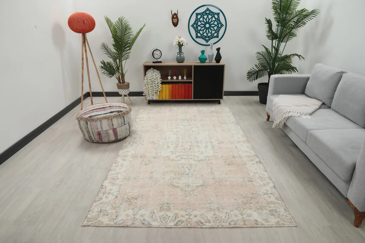 Vintage rug displayed in a living room setting, showing its scale and light colors with furniture.