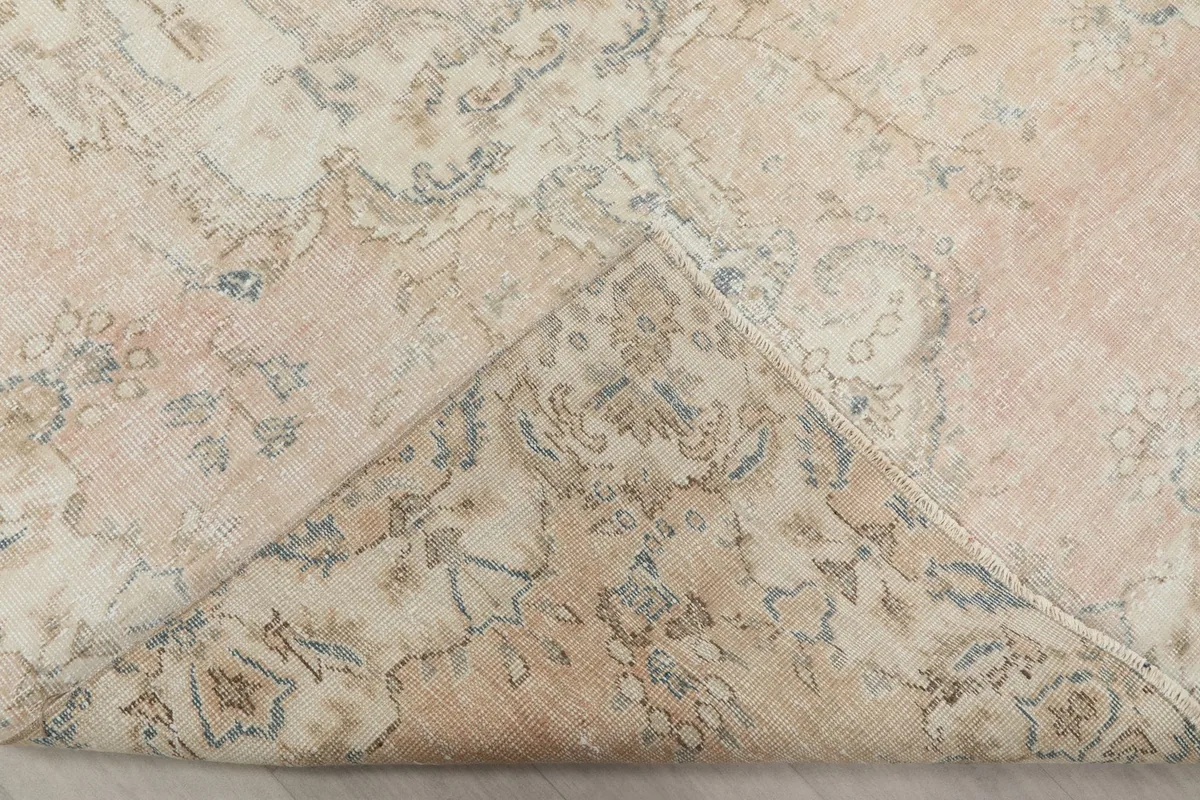 Corner of the rug folded back, revealing the cotton foundation and the reverse of the hand-knotted pile.