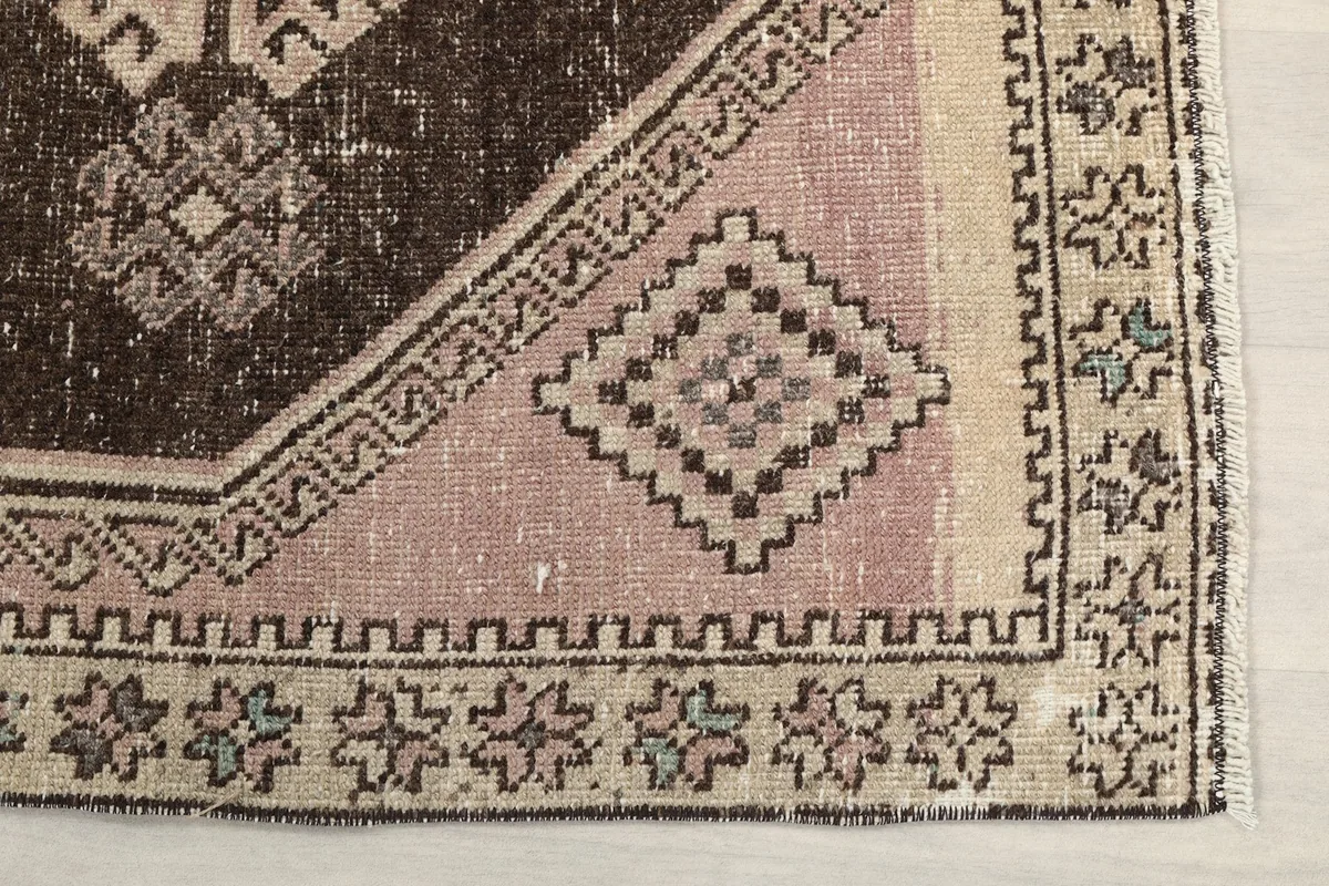 Detailed view of the rug's corner, highlighting the pink field, beige border, and small floral motifs.
