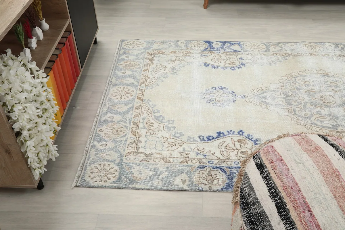 Angle view of the rug's end, showing the border and part of the central design next to a decorative pouf.