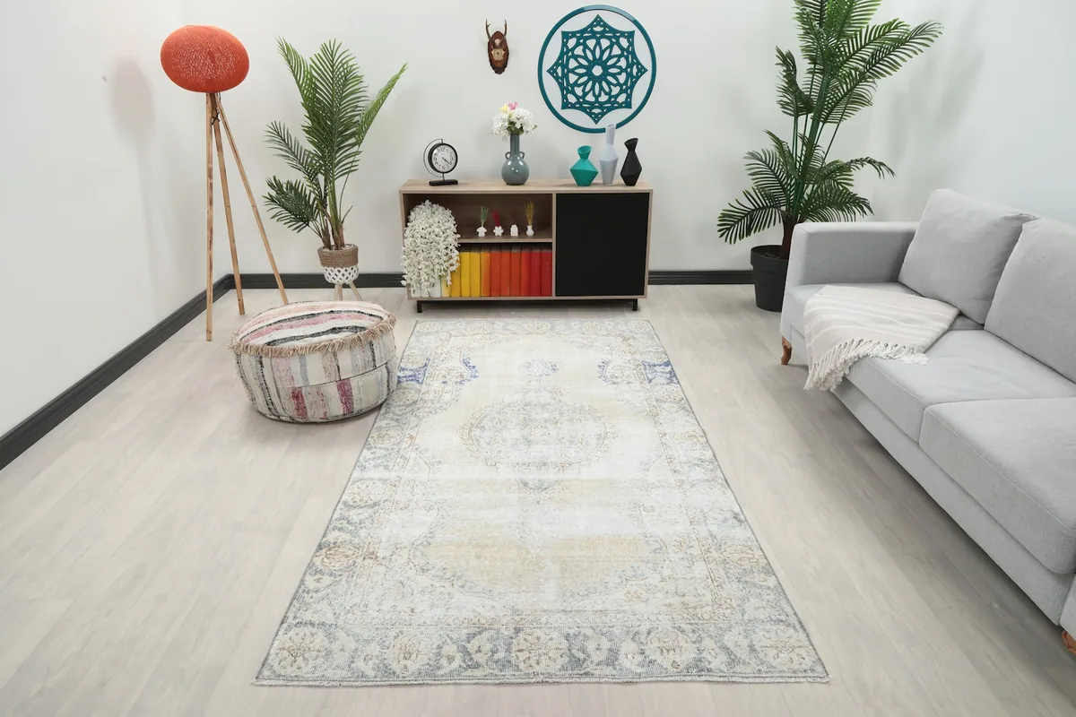 Vintage ivory and blue area rug displayed in a modern living room setting with a gray sofa and wooden cabinet.