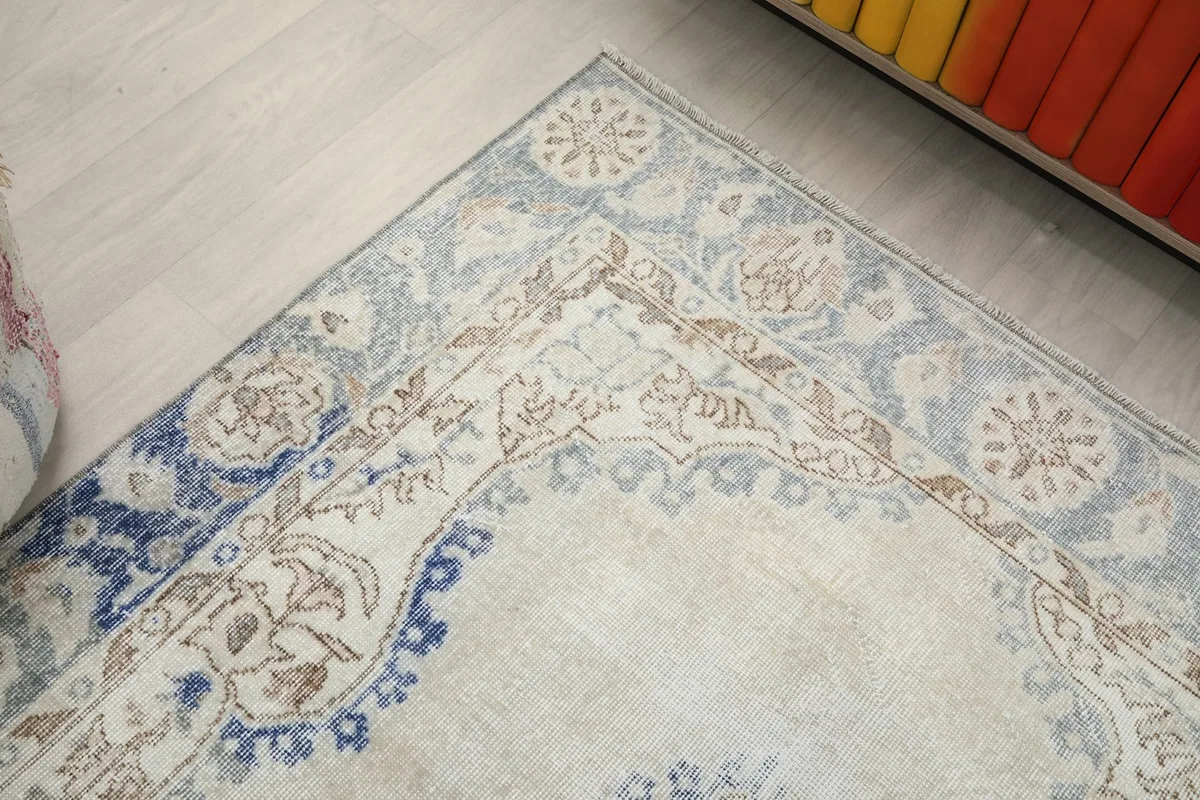 Corner detail of the rug, showing the blend of ivory, blue, and tan in its floral border design.