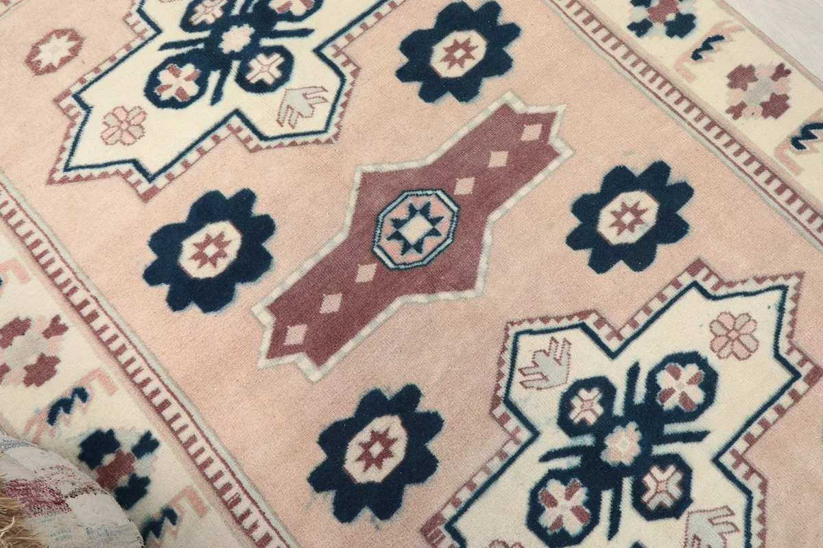 Close-up of the central section of the rug, showing navy and ivory geometric designs on a rose field