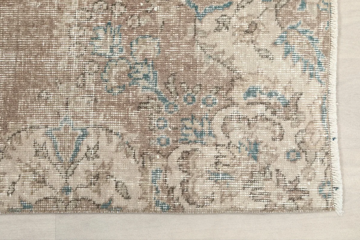 Detailed view of the rug's corner, showing faded tan, blue, and cream floral motifs