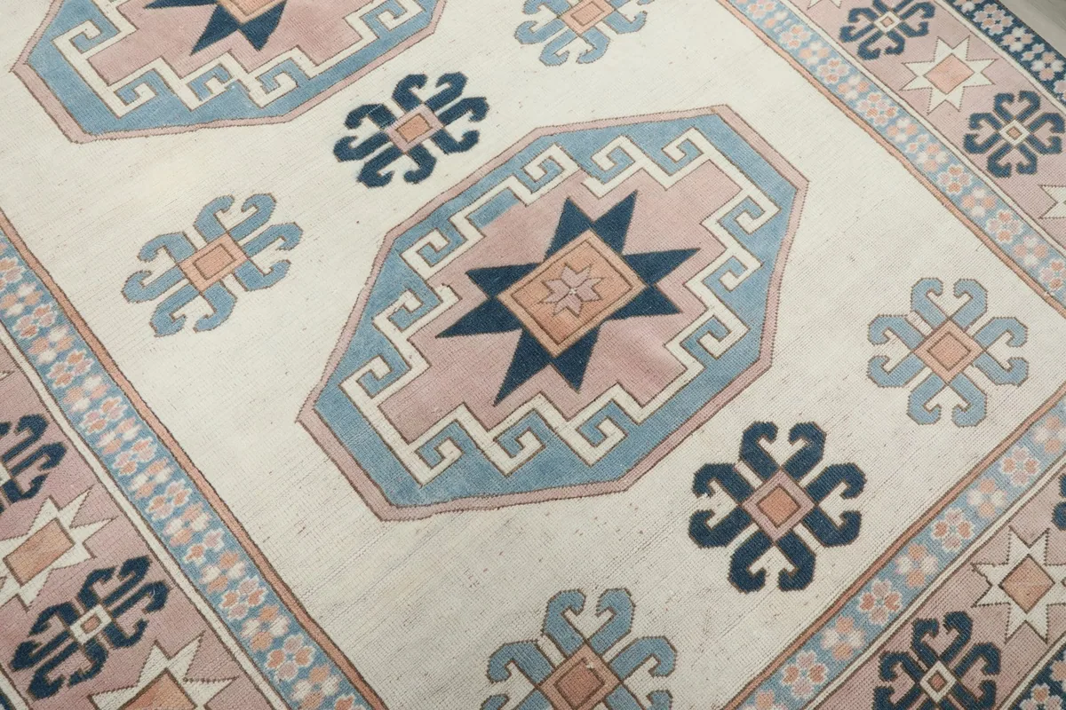 Close-up of a main geometric medallion in pink and blue on the ivory field.