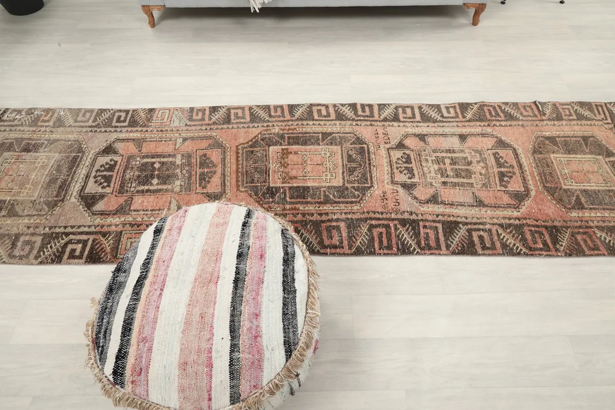 Full length view of the rose and charcoal runner rug on a light floor, with an ottoman