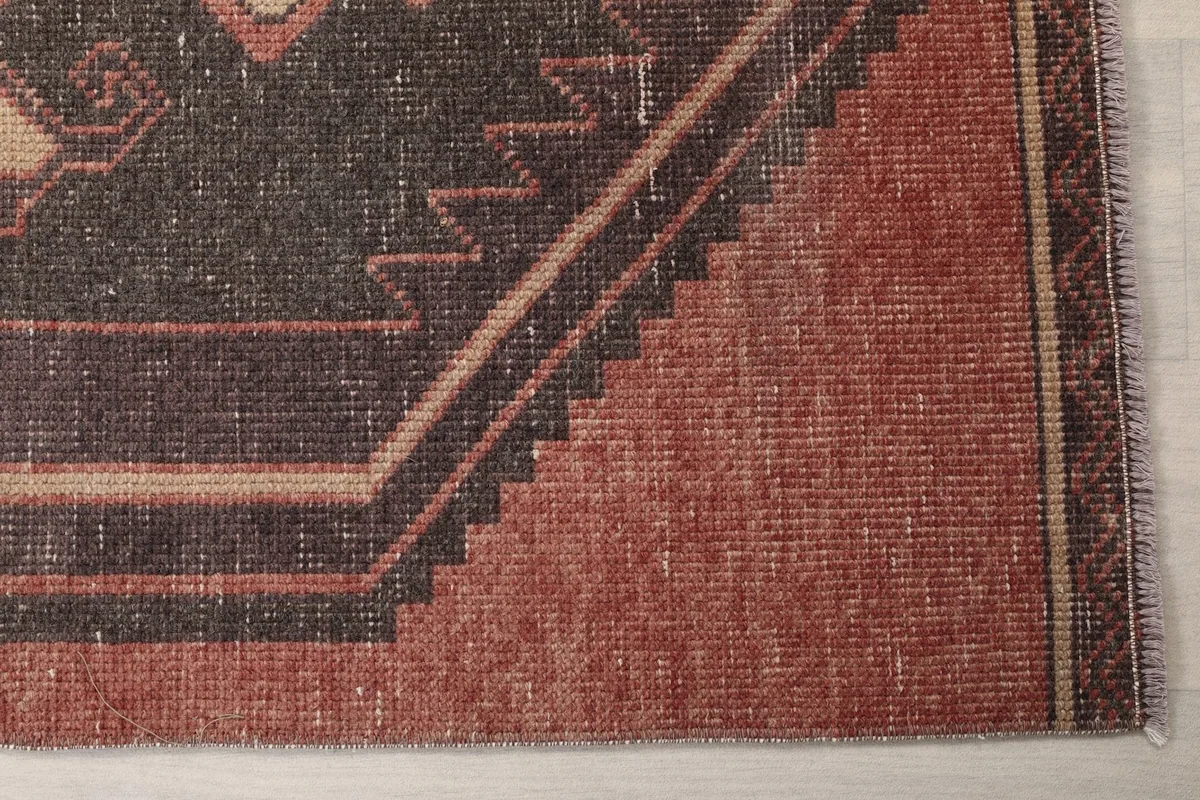 Detailed view of the rug's edge, showing the rust color and subtle geometric border patterns.
