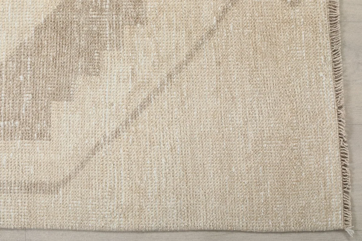 Close-up detail of the cream field and tan geometric border, showing the hand-knotted texture and low pile.