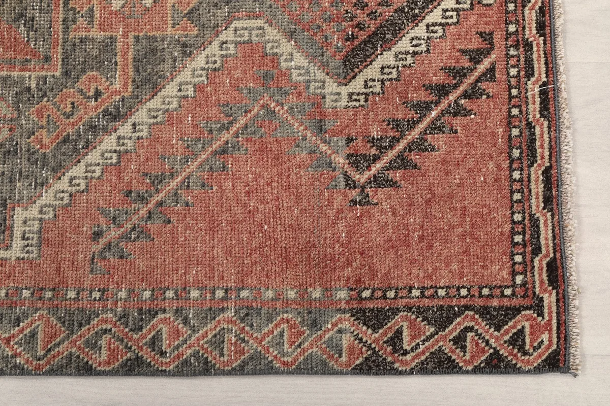 Detail of the corner showing the rust field and charcoal border with geometric motifs