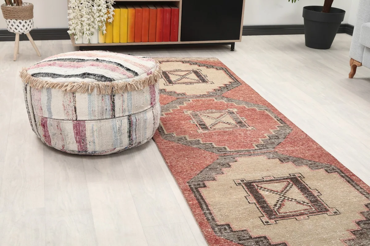 Close-up view of the rust and beige runner rug's pattern next to a round ottoman