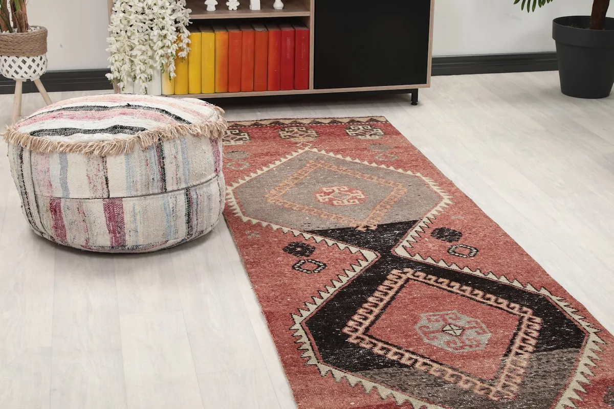 Close-up view of one end of the runner rug in a room, with a decorative pouf nearby