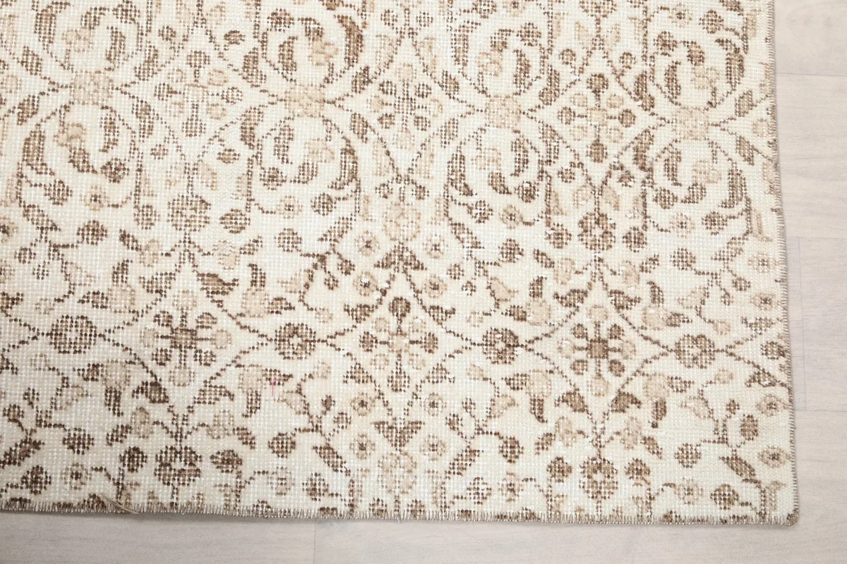 Detailed view of the intricate brown floral and geometric motifs on the cream background of the rug.
