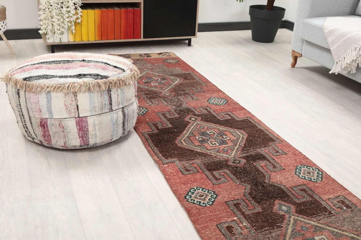 Close-up angled view of the runner rug showing its texture and colors next to a striped pouf.