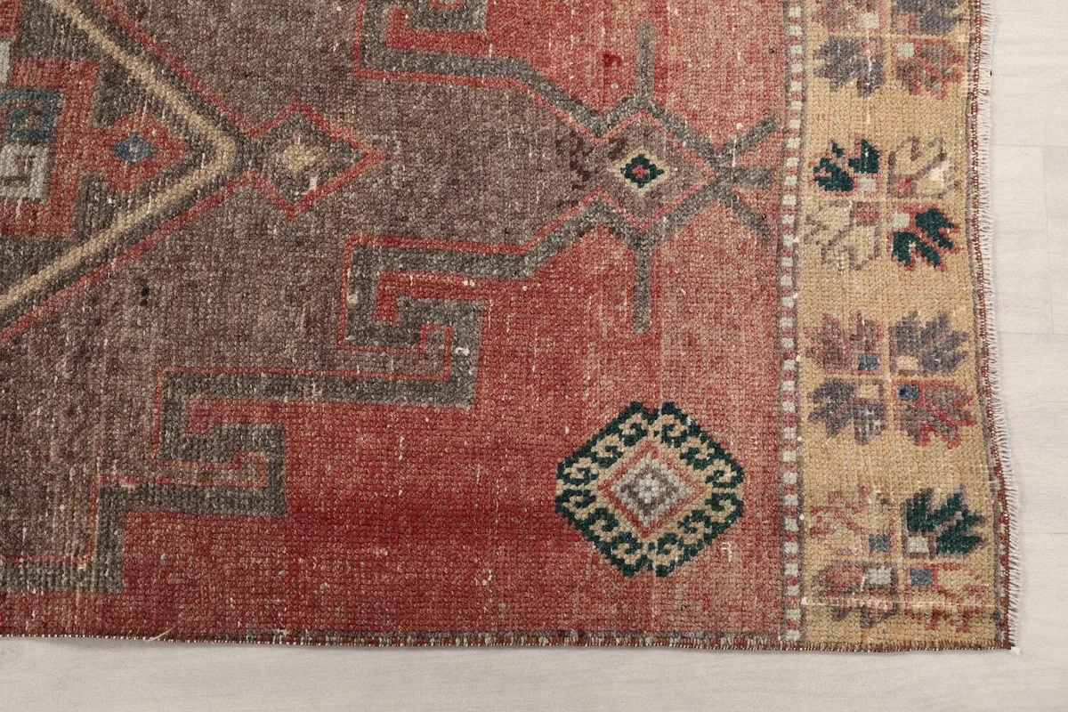 Detailed view of the rug's rust field, brown geometric motifs, and beige border with small designs.