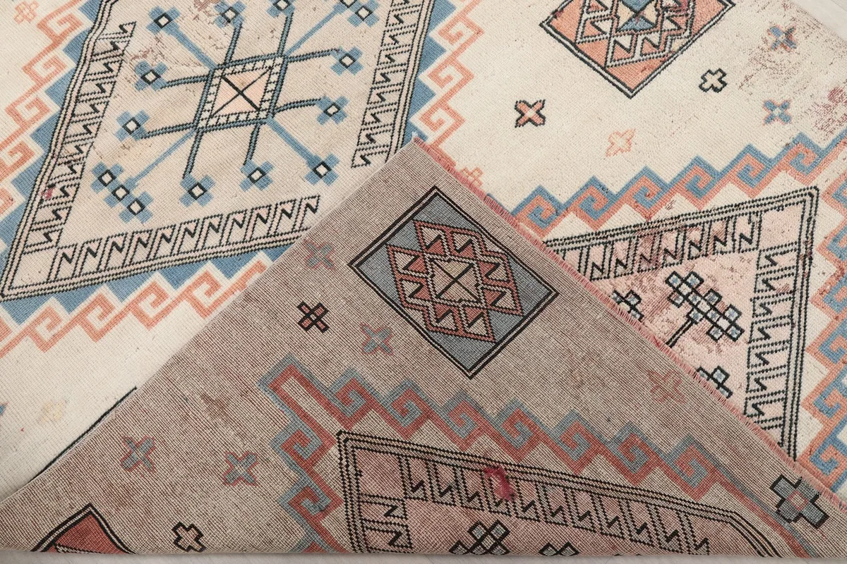 Corner of the rug folded back, revealing the reverse side and hand-knotted foundation.