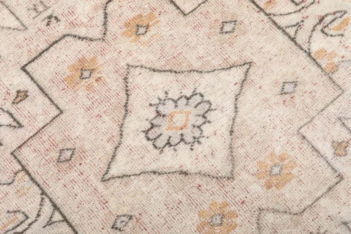 Macro detail of the hand-knotted texture and faded rose and gold threads within the medallion