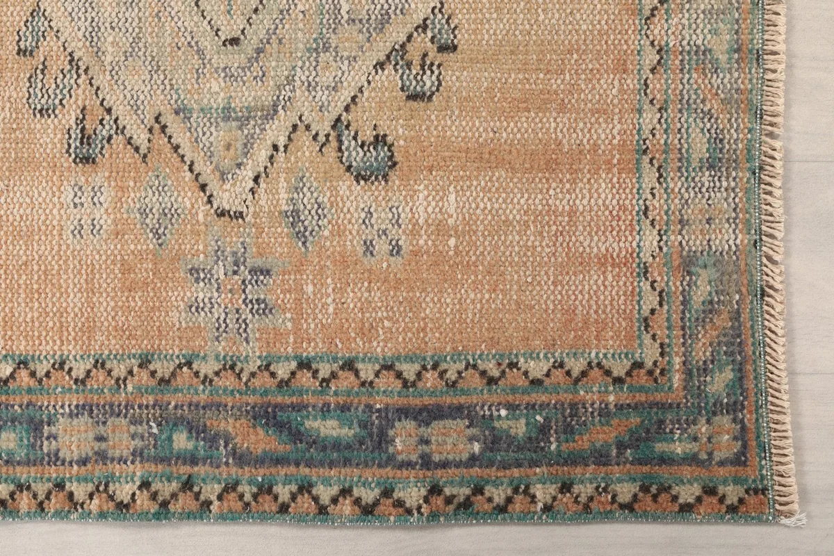 Detail shot of the corner of the rug, highlighting the faded blue and rust tones in the border pattern.