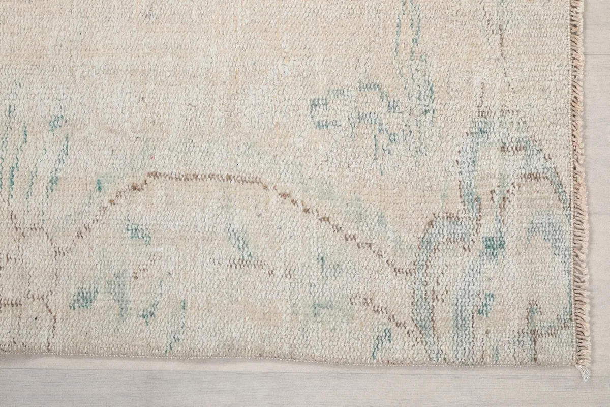 Detailed view of the rug's border showing the faded blue and tan floral motifs and weave.