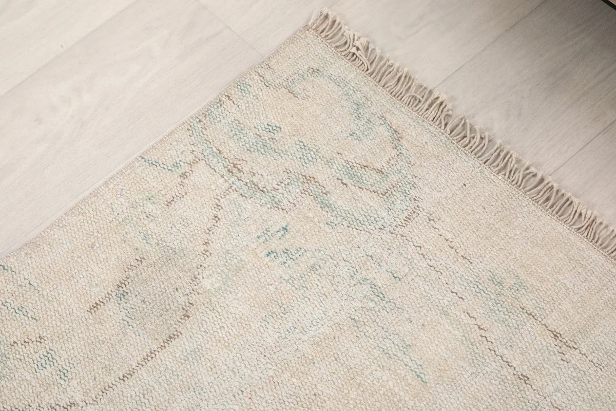 Corner detail of the rug's border and fringe, showing the intricate faded patterns.