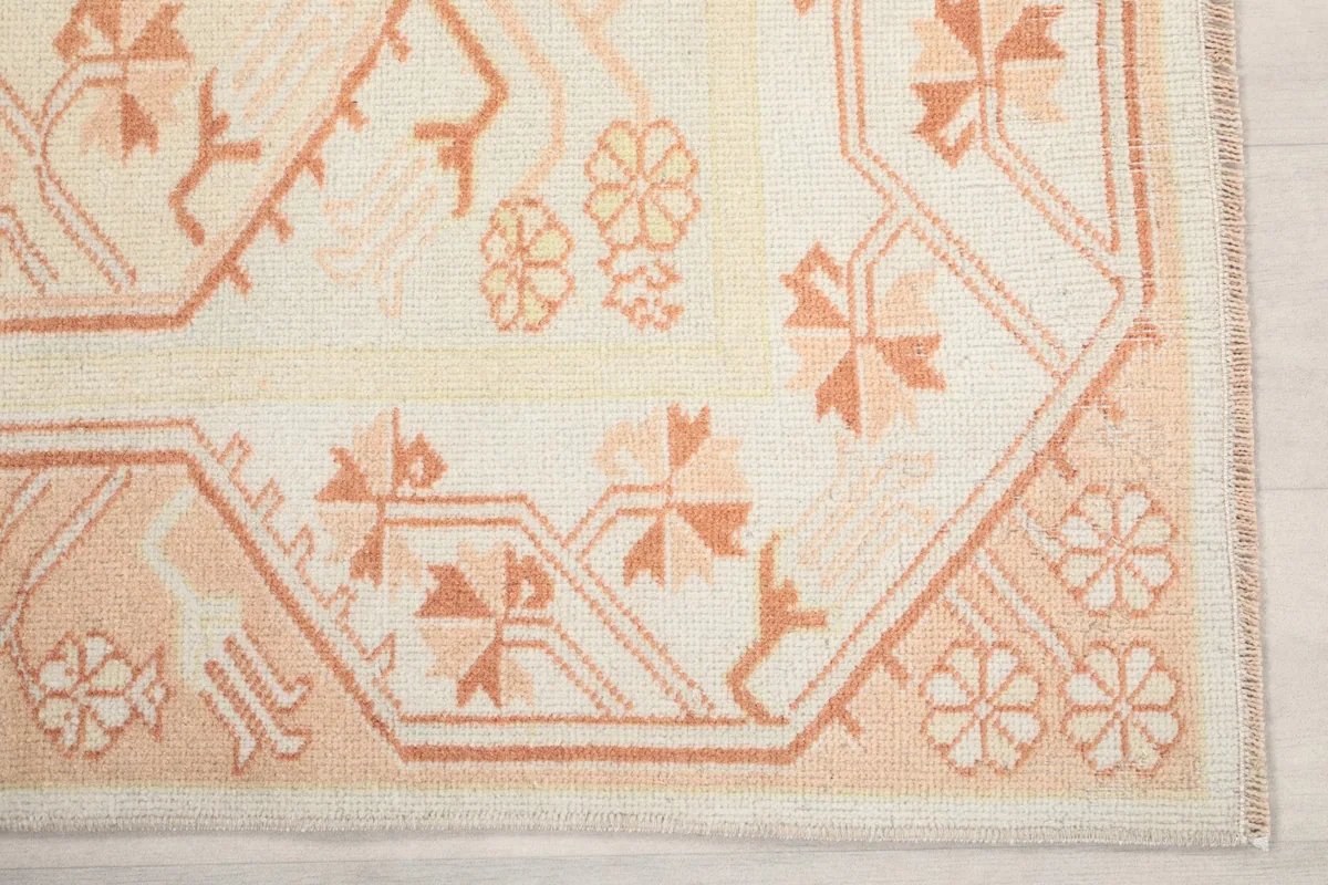 Detailed view of the corner of the rug, showcasing the intricate geometric and floral patterns in cream and orange.