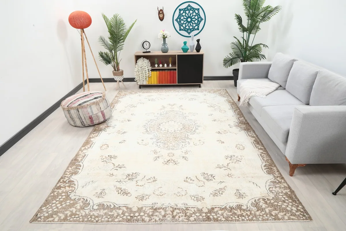 Ivory and tan rug displayed in a living room setting with a light gray sofa and plants