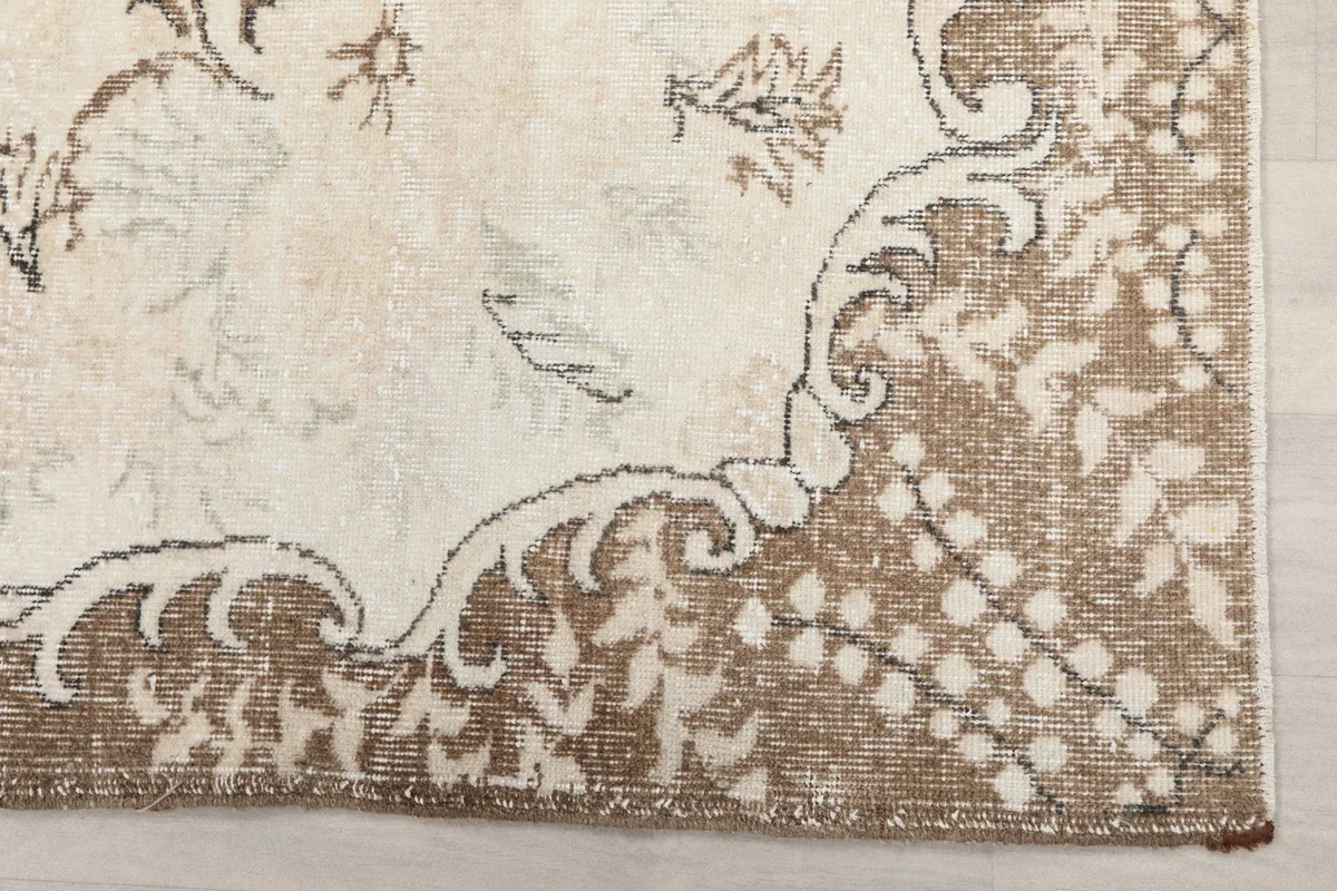 Detail of the tan and brown border design with faded patterns on the ivory rug