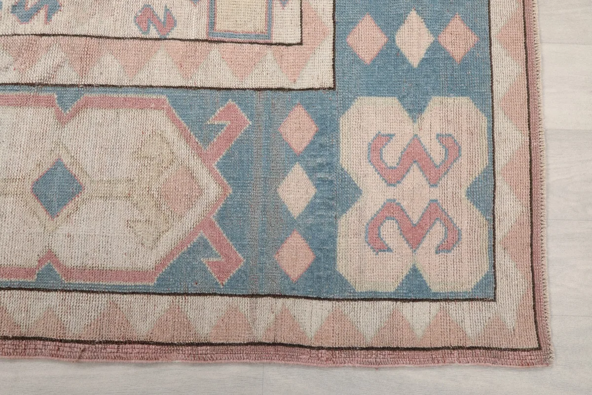 Detail of the blue border with ivory and pink geometric motifs, showing the edge of the rug