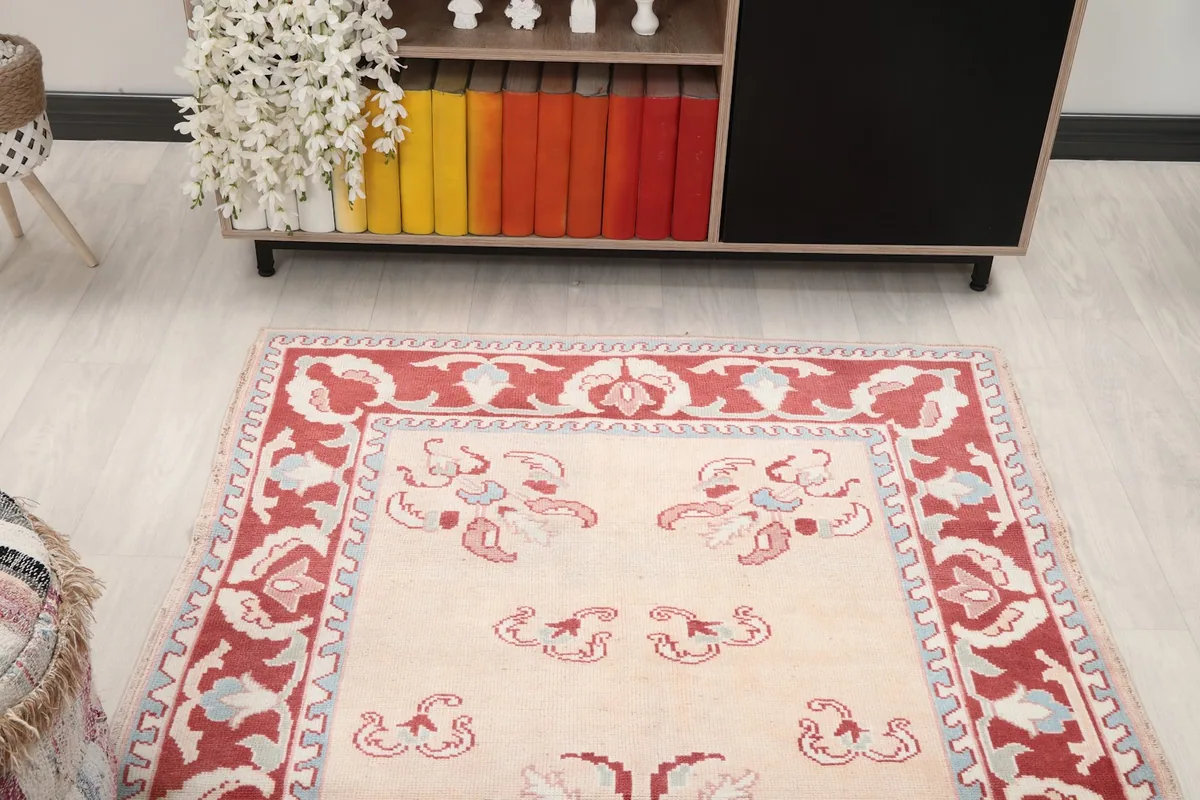 Angled view of the rug's top half, showing the beige field and red border pattern in a room setting.