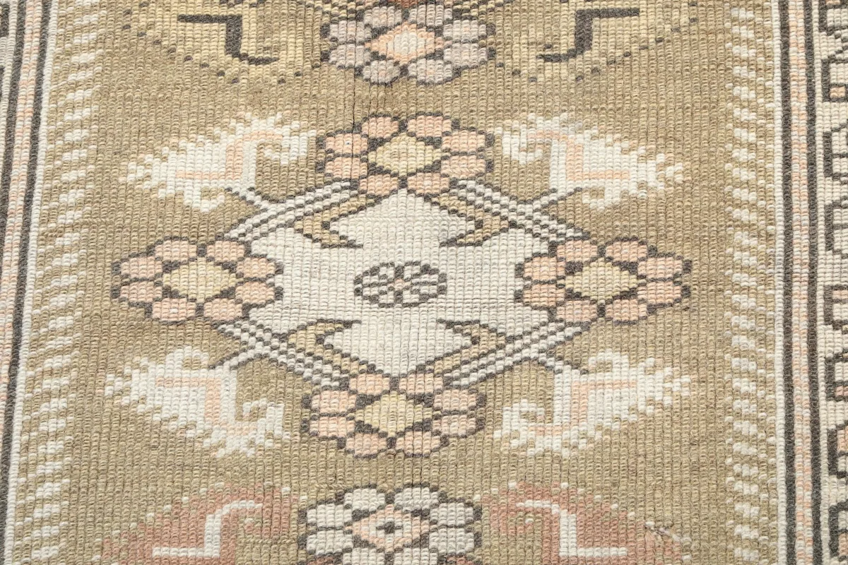 Close-up of a central geometric motif in beige, pink, and brown on the rug