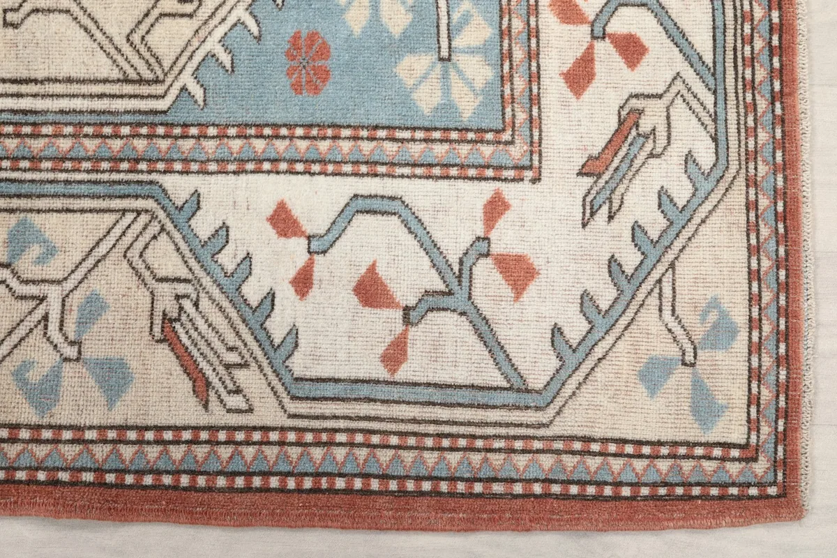 Detailed view of the beige border with blue and rust tribal patterns on the vintage rug