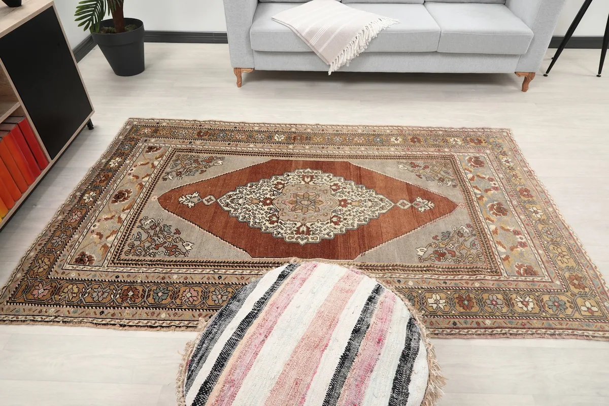 Full view of the rust and gray vintage rug in a living room, with a striped ottoman in the foreground