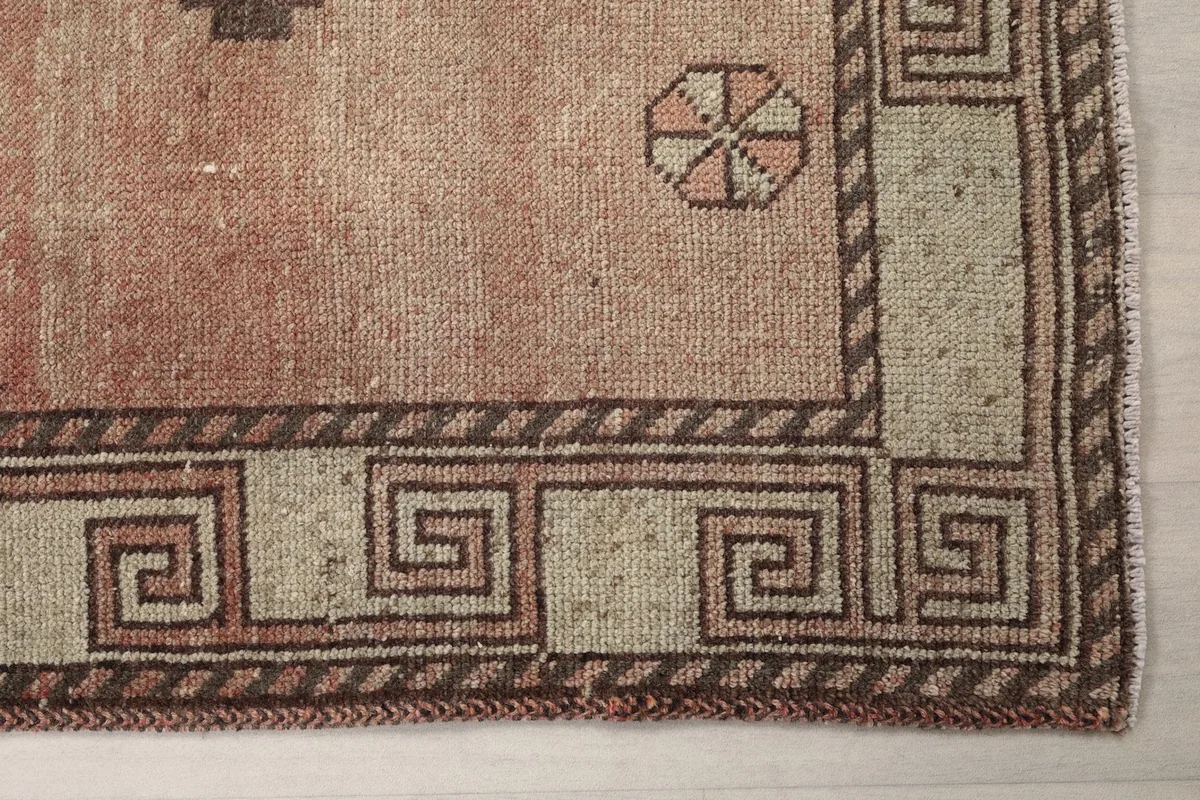 Detailed view of the rug's beige border with a Greek key pattern and a small circular motif on the rust field.