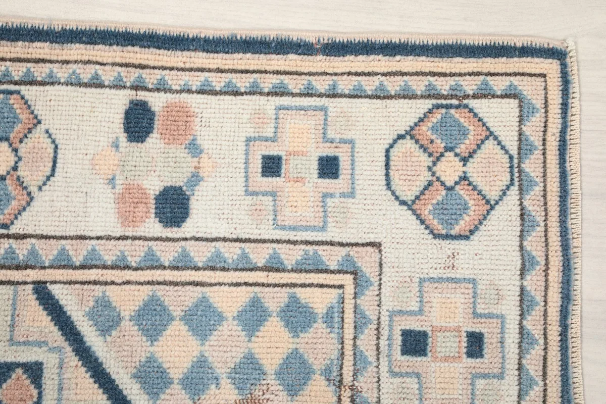 Detailed view of the rug's corner with various geometric motifs in blue, tan, and rose
