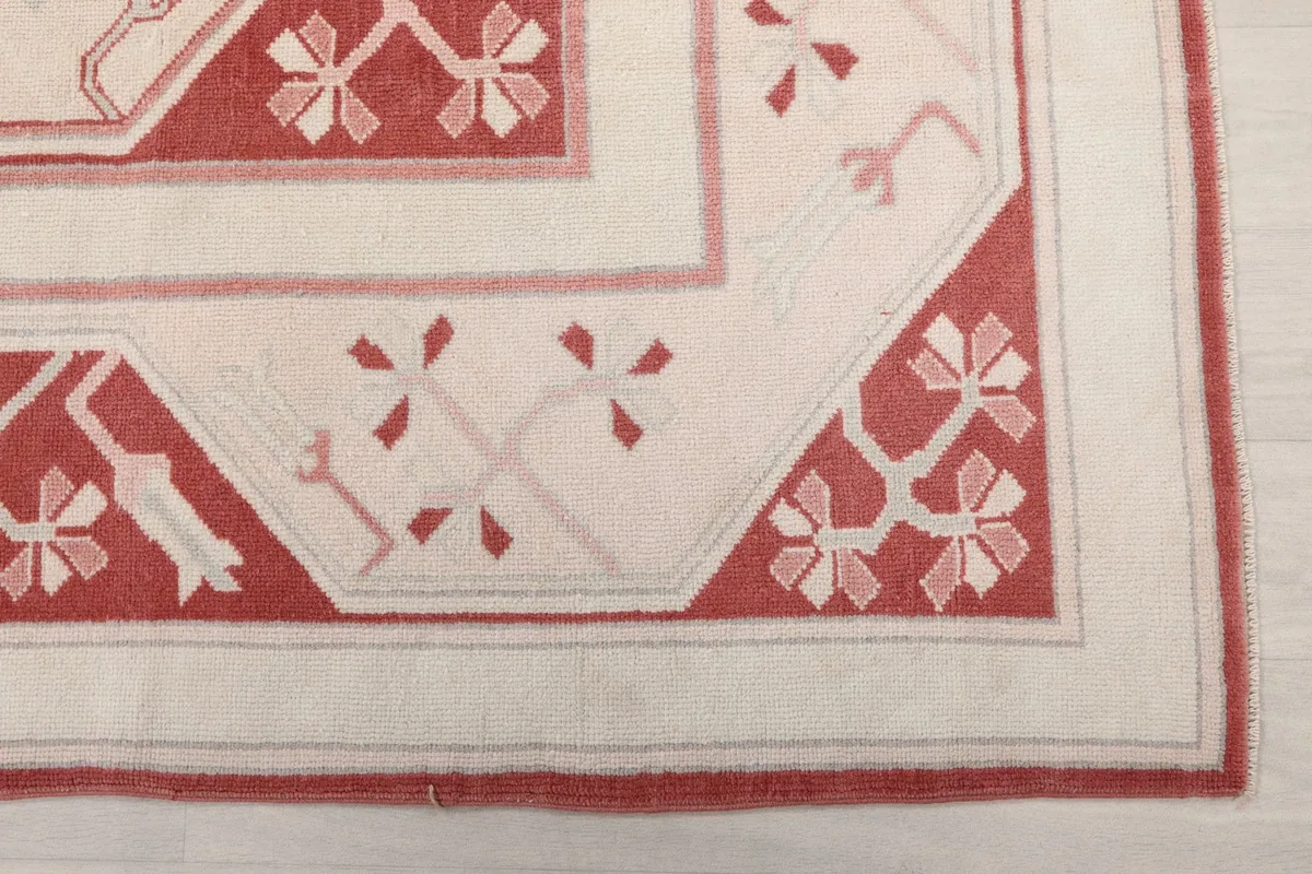Detailed corner view of the rug, highlighting the cream border and rose geometric motifs.