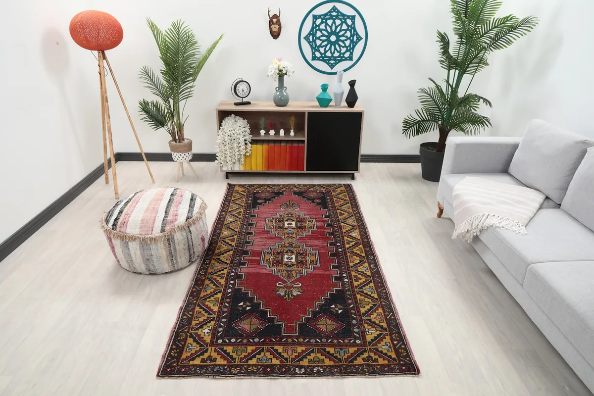 Vintage red and gold Anatolian rug placed in a living room setting with a light gray sofa and wooden furniture.