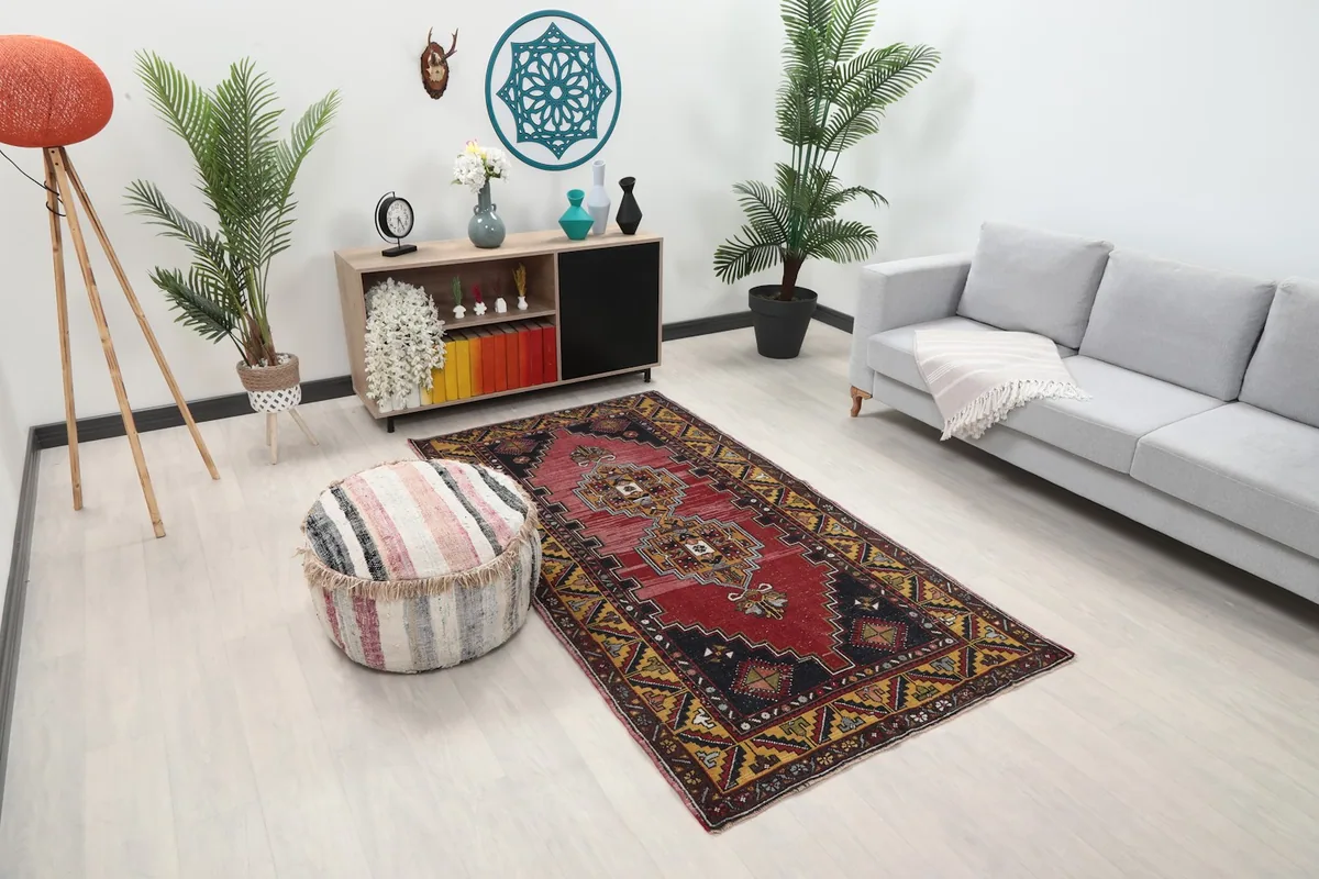 Angled view of the red and gold Anatolian rug in a room, showing its placement near a sofa and a striped pouf.