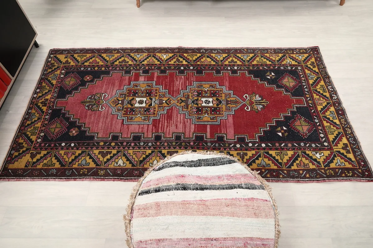 Full overhead view of the red and gold Anatolian rug in a room setting, with a striped pouf.