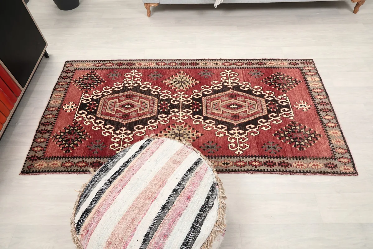Full room view of the red area rug with a striped pouf in the foreground
