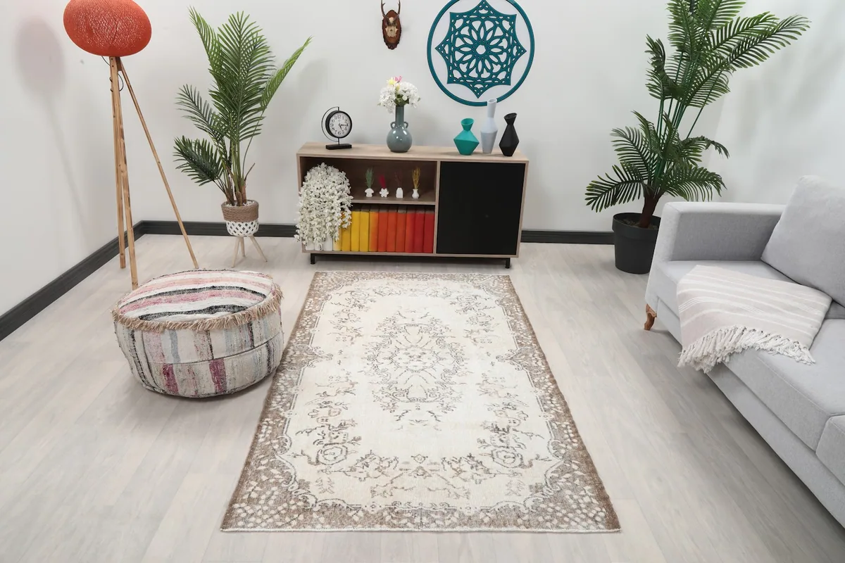 Cream floral medallion rug placed in a modern living room setting with a couch and pouf
