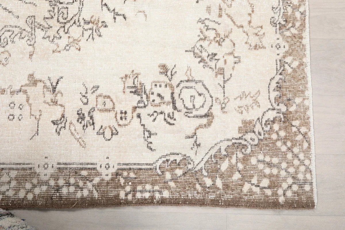 Close-up detail of the rug's brown border and a corner of the cream field with floral motifs