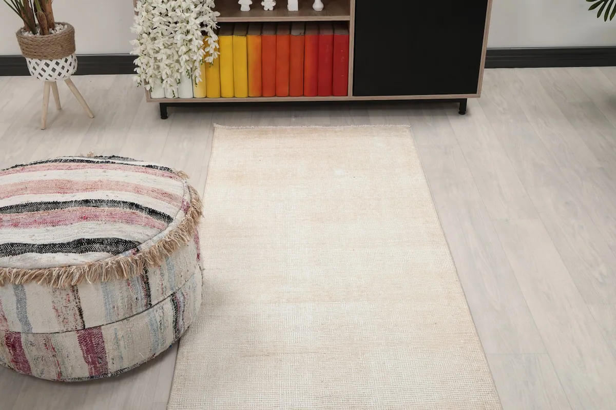 Overhead view of a section of the beige runner rug in a room, with a pouf and cabinet.
