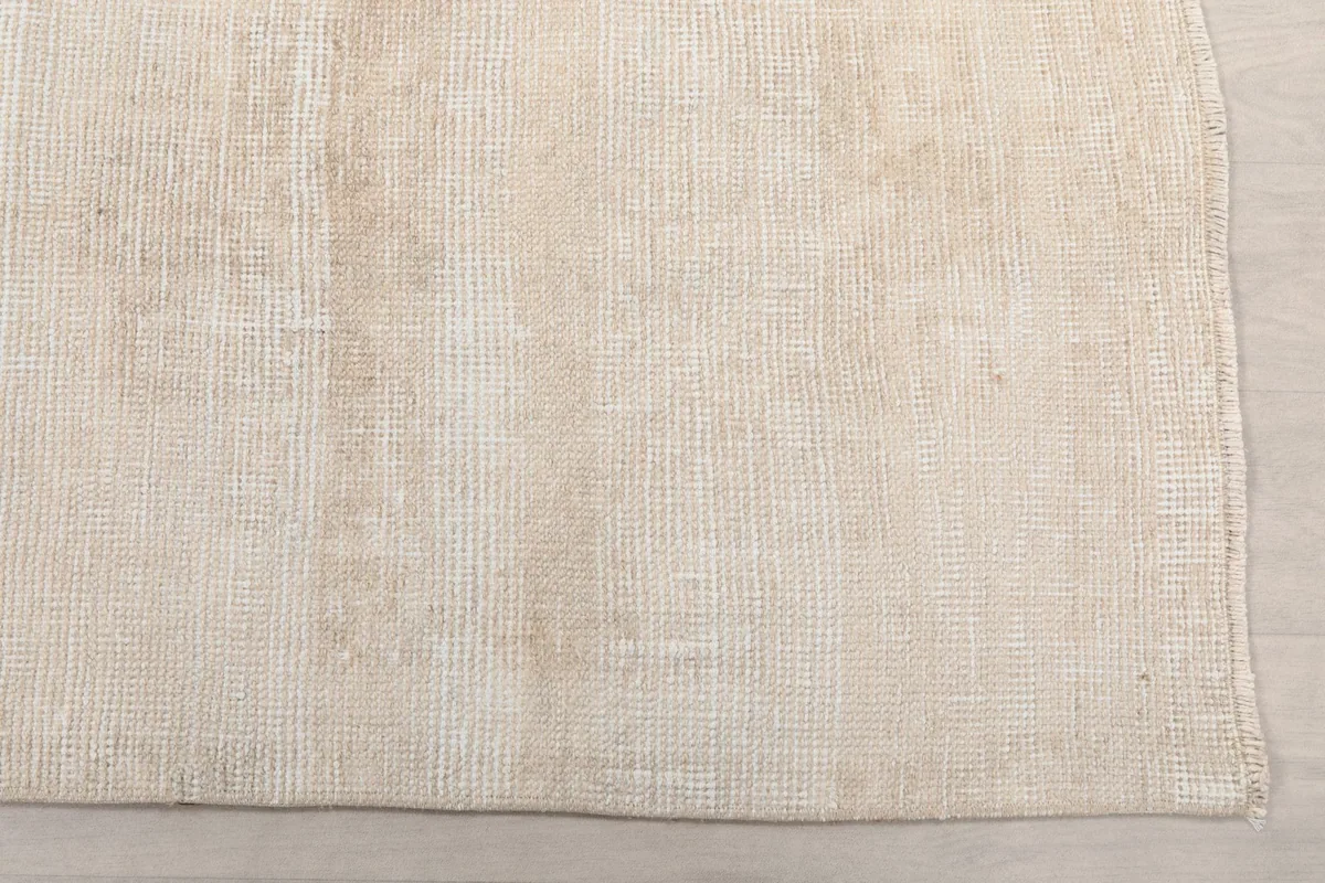 Close-up detail of the rug's surface, showing the beige and cream wool pile texture and slight fading.