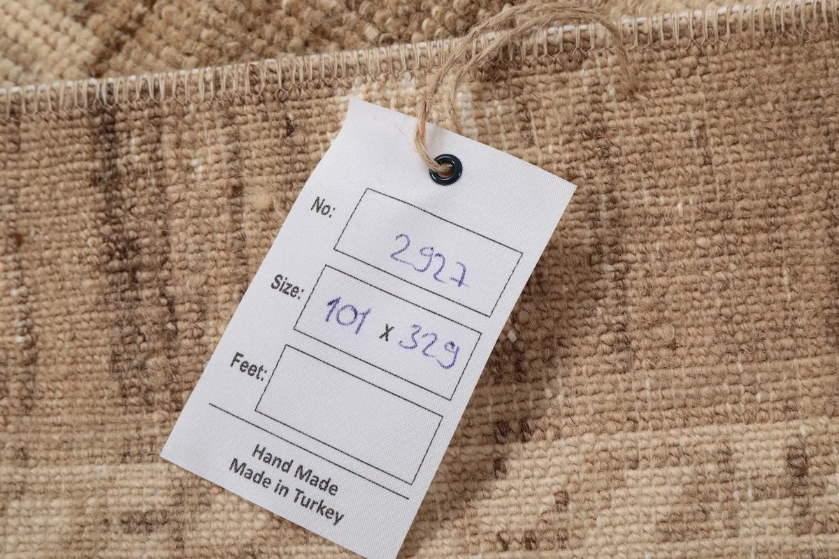Close-up of the rug's label, indicating hand-made in Turkey and size 101 x 329 cm