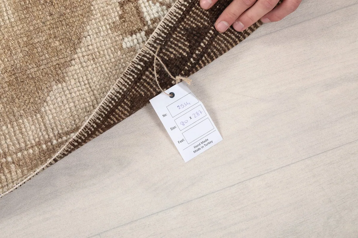 Hand holding a product tag against the back of the rug, showing its origin and material
