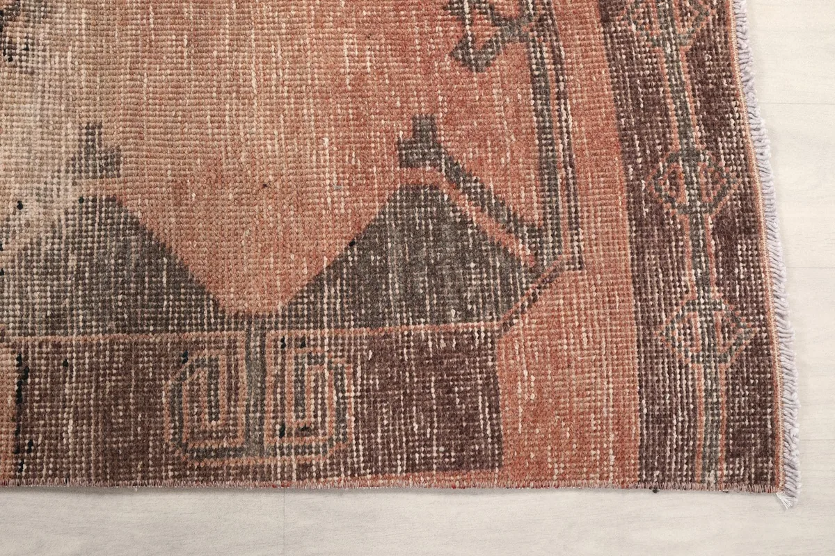 Detailed view of the corner of the vintage rug, showing the faded rust and brown colors