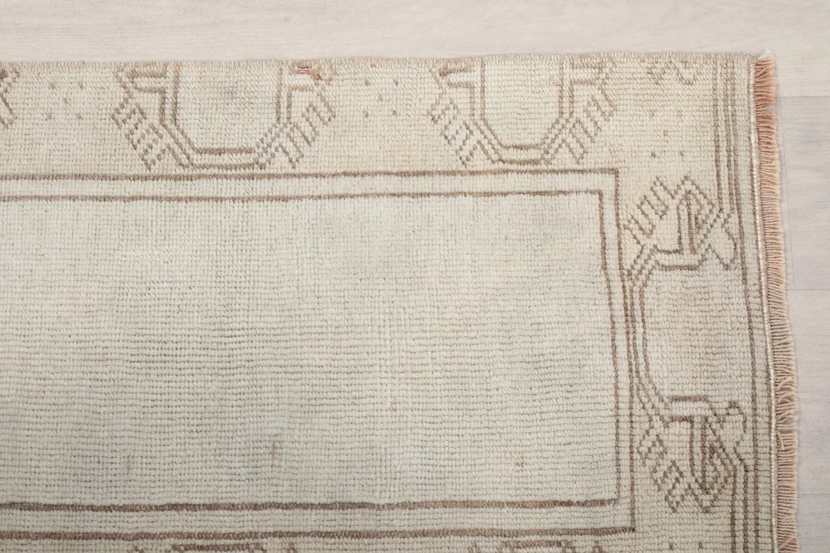 Detailed view of the cream field and the beige geometric patterns along the border of the runner rug.