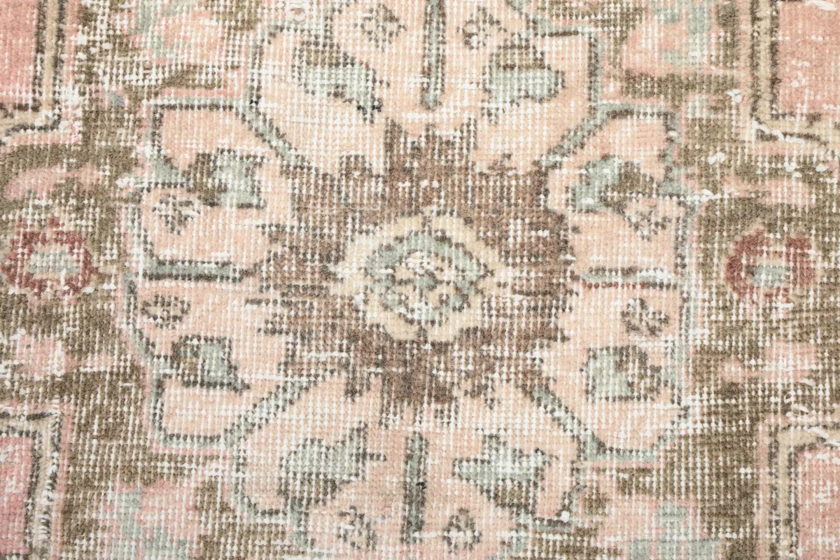 Texture detail of the low pile and faded rose, brown, and beige colors of the rug