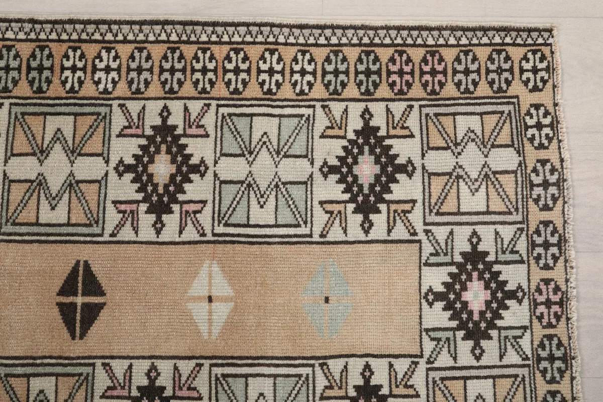 Detailed view of the rug's geometric patterns and colors, including tan, rust, black, and gray.
